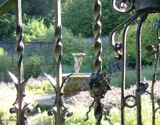 9309434_orig Seen through the bars of a ornate wrought iron gate, a fountain in the walled garden is visible, in front of a fruitcage and shrubs